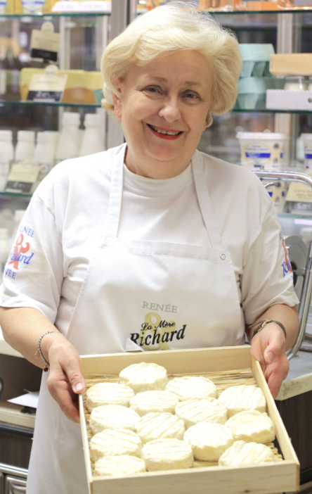 La Mère Richard dans sa fromagerie, tenant un plateau de fromages