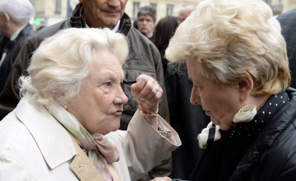 La Mère Richard échange avec un passant dans la rue, transmettant son savoir et sa passion pour la cuisine lyonnaise, image d’une tradition vivante et partagée.